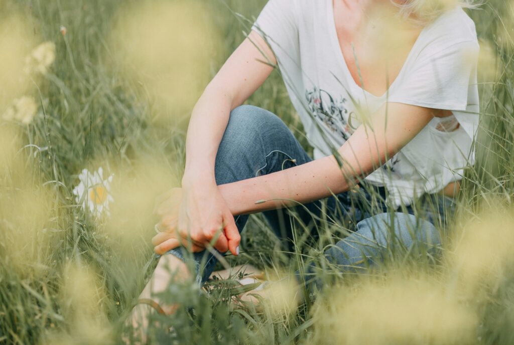 Unrecognizable woman sitting in a lush meadow filled with daisies, enjoying nature.