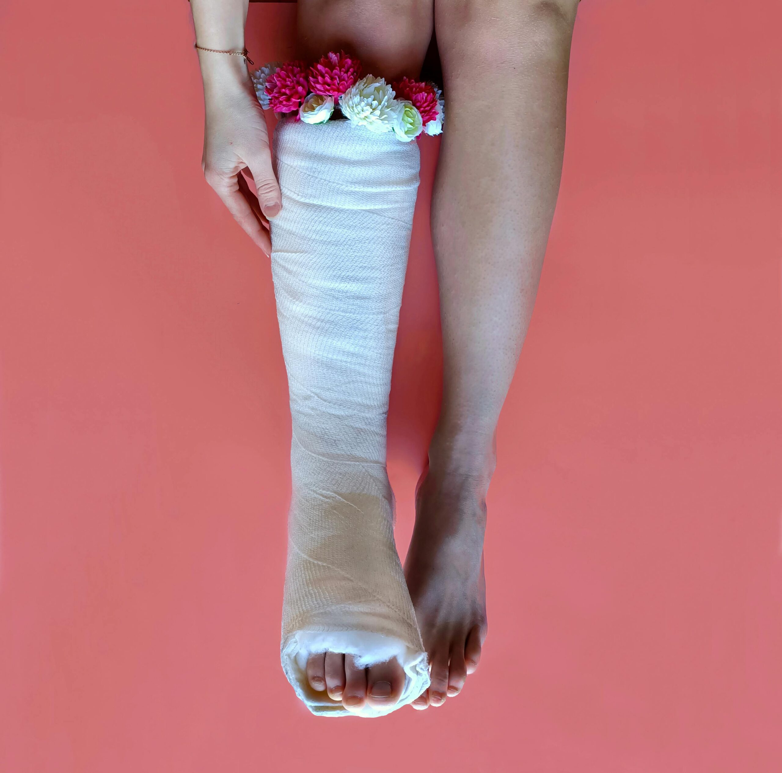 A leg with a cast adorned with colorful flowers on a pink background, blending beauty and recovery.