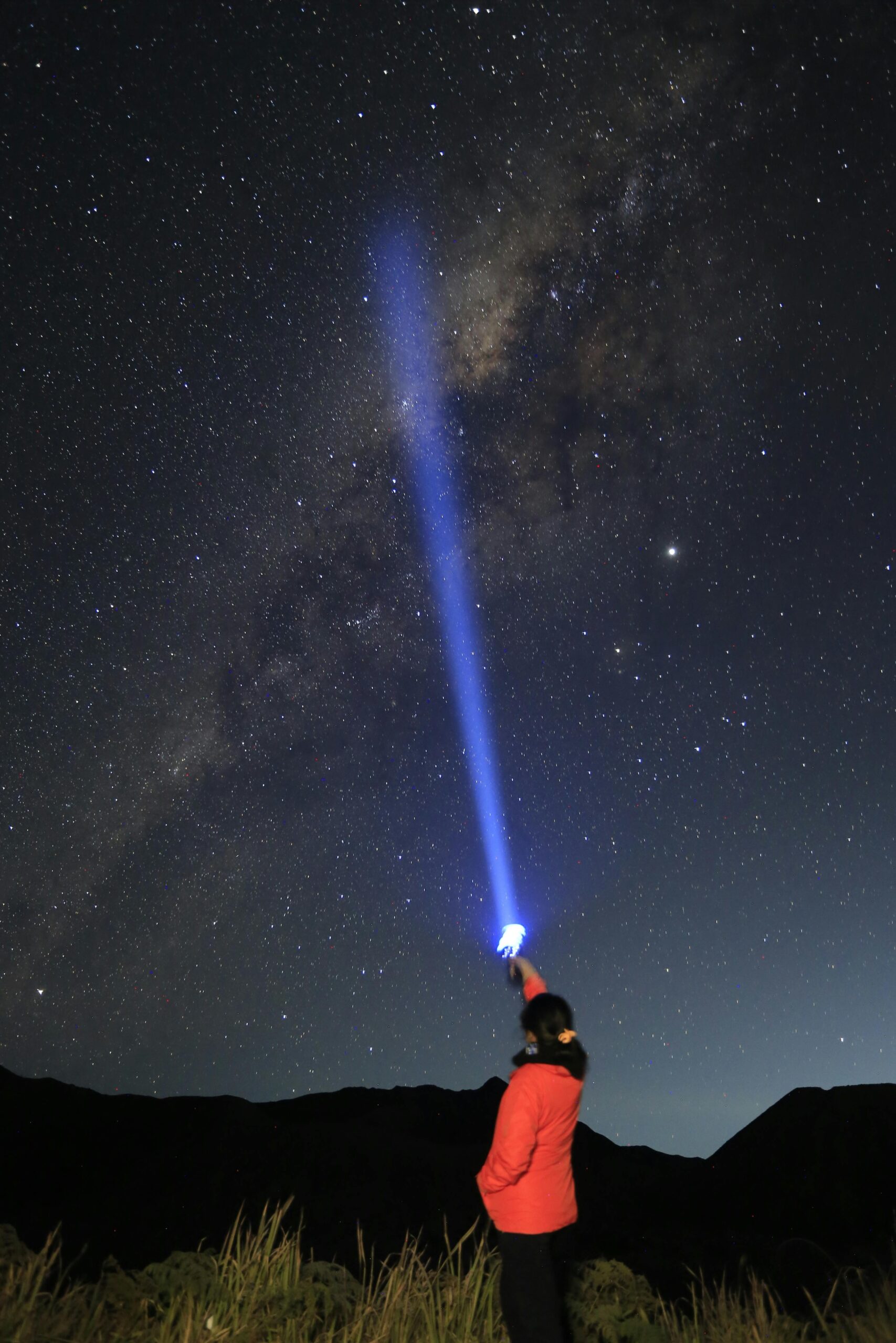 A woman uses a flashlight to point at the stunning Milky Way under a clear night sky.