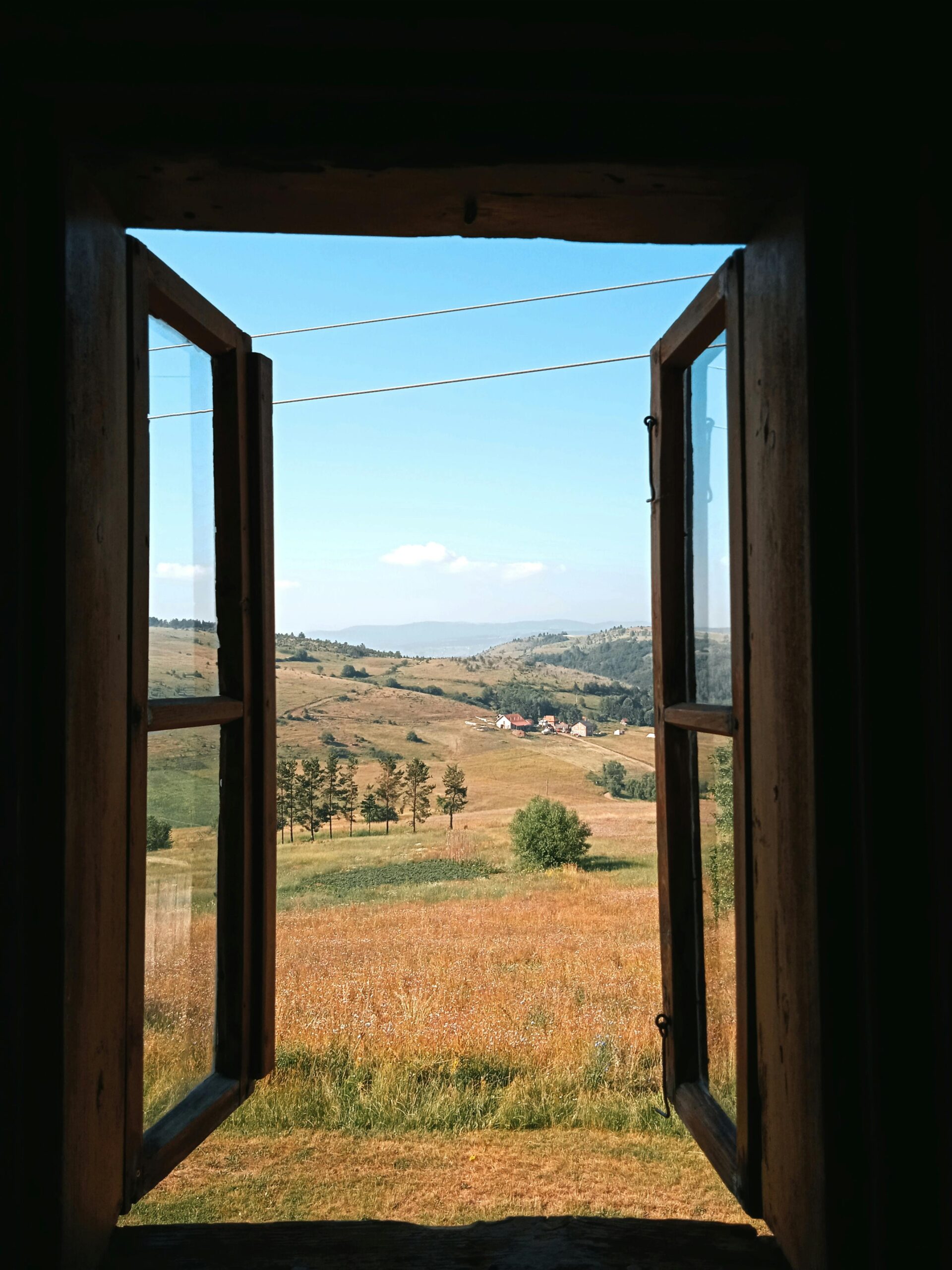 Scenic rural landscape viewed through a wooden open window, capturing a tranquil nature scene.
