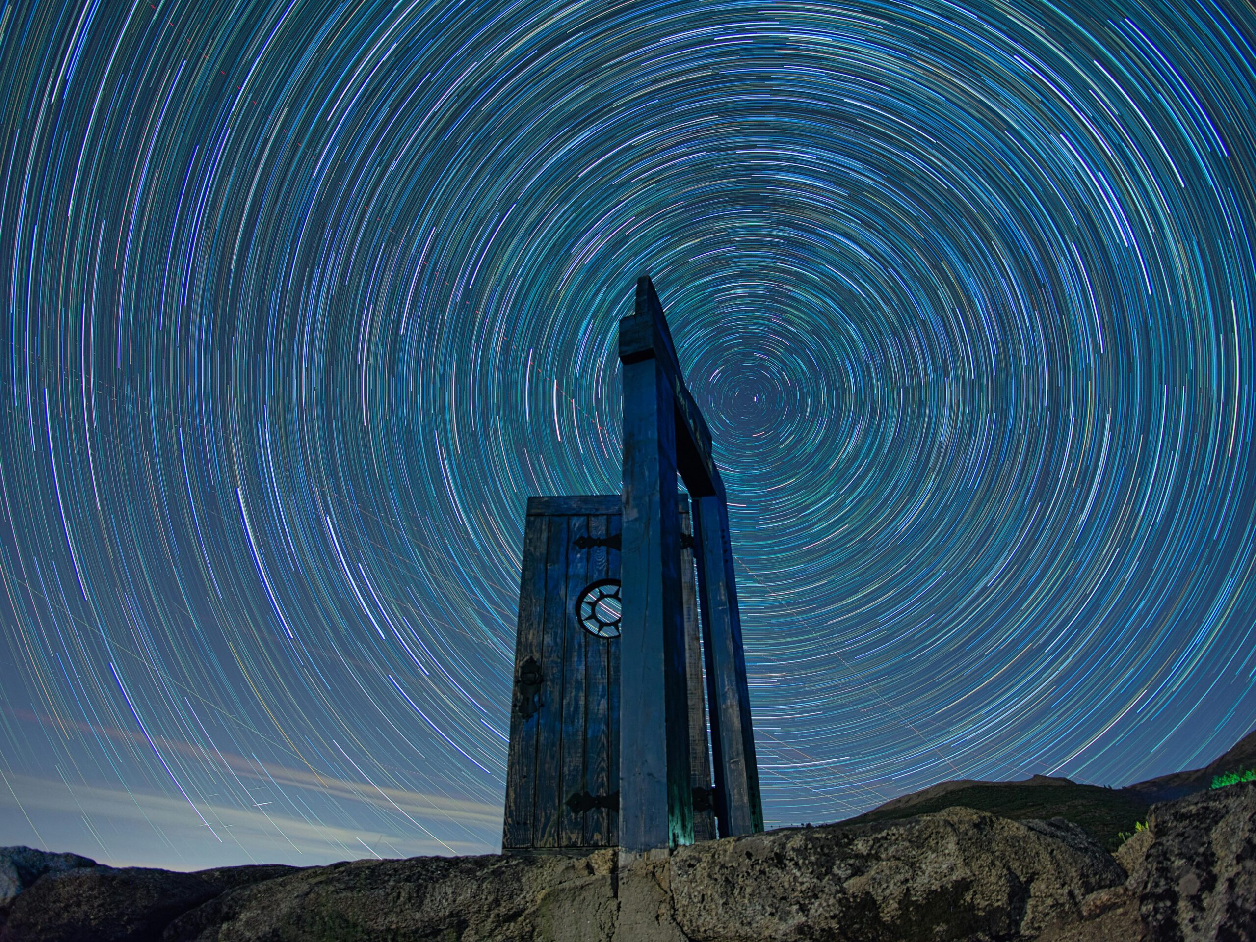 Dramatic star trail swirls over a mountain monument captured in a long exposure night sky.